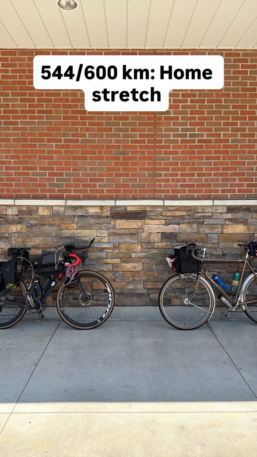 Two loaded brevet bikes leaning against a brick wall outside a convenience store, captioned 544 of 600 km: home stretch